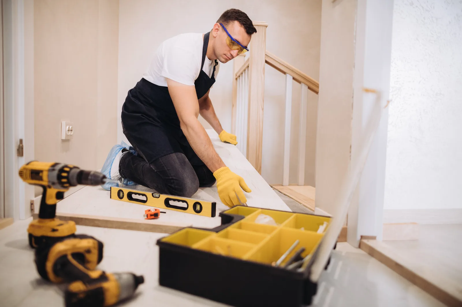 A tradesperson fits flooring with a level and tools nearby